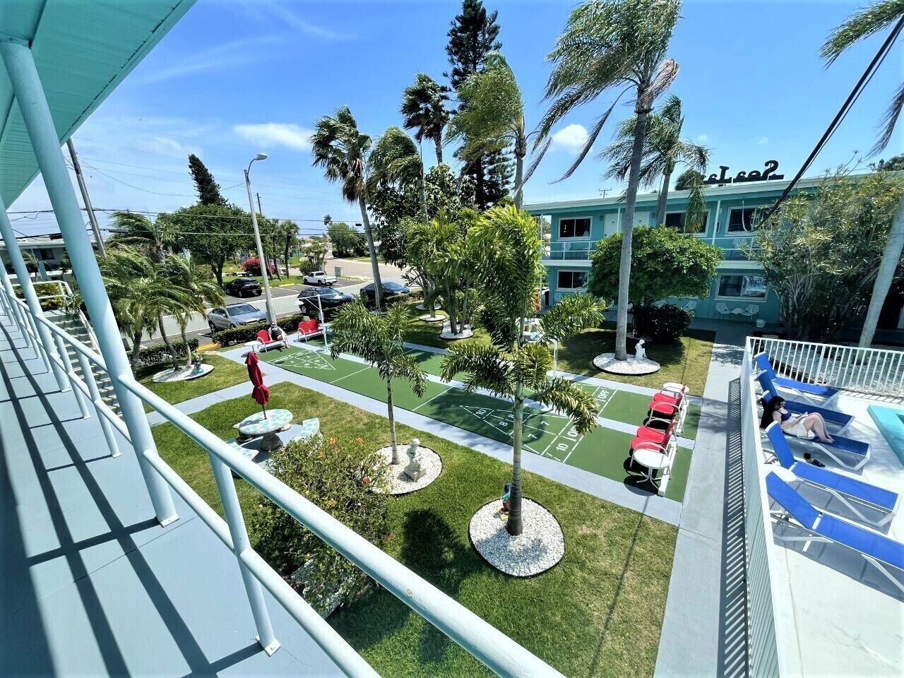 Een hotel met een zwembad, terras en palmbomen.