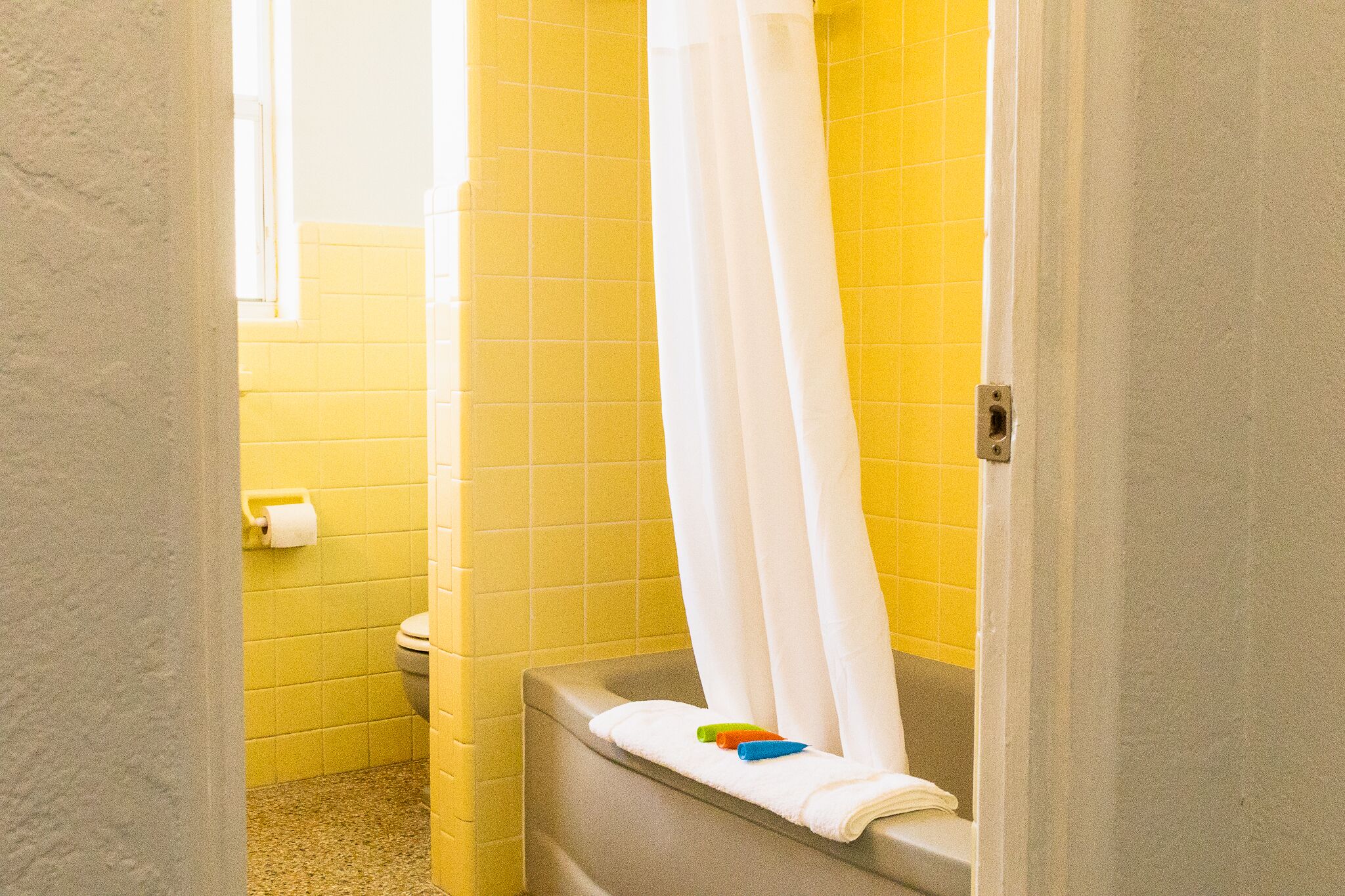 A bathroom with yellow tiles, a white toilet, and a bathtub with a white shower curtain.