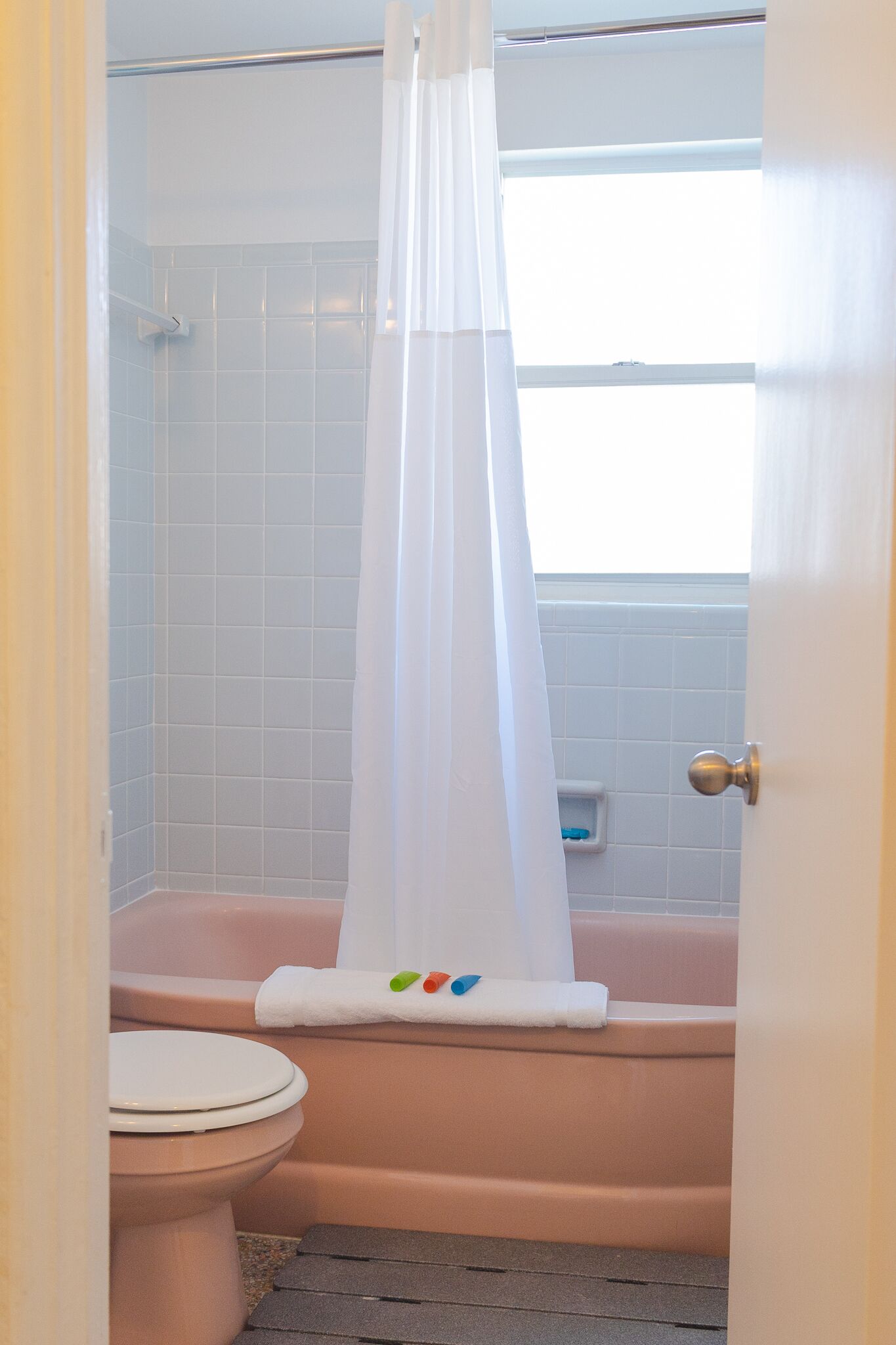 Ein Badezimmer mit einer rosa Badewanne, einer weißen Toilette und einer Duschvorhang.