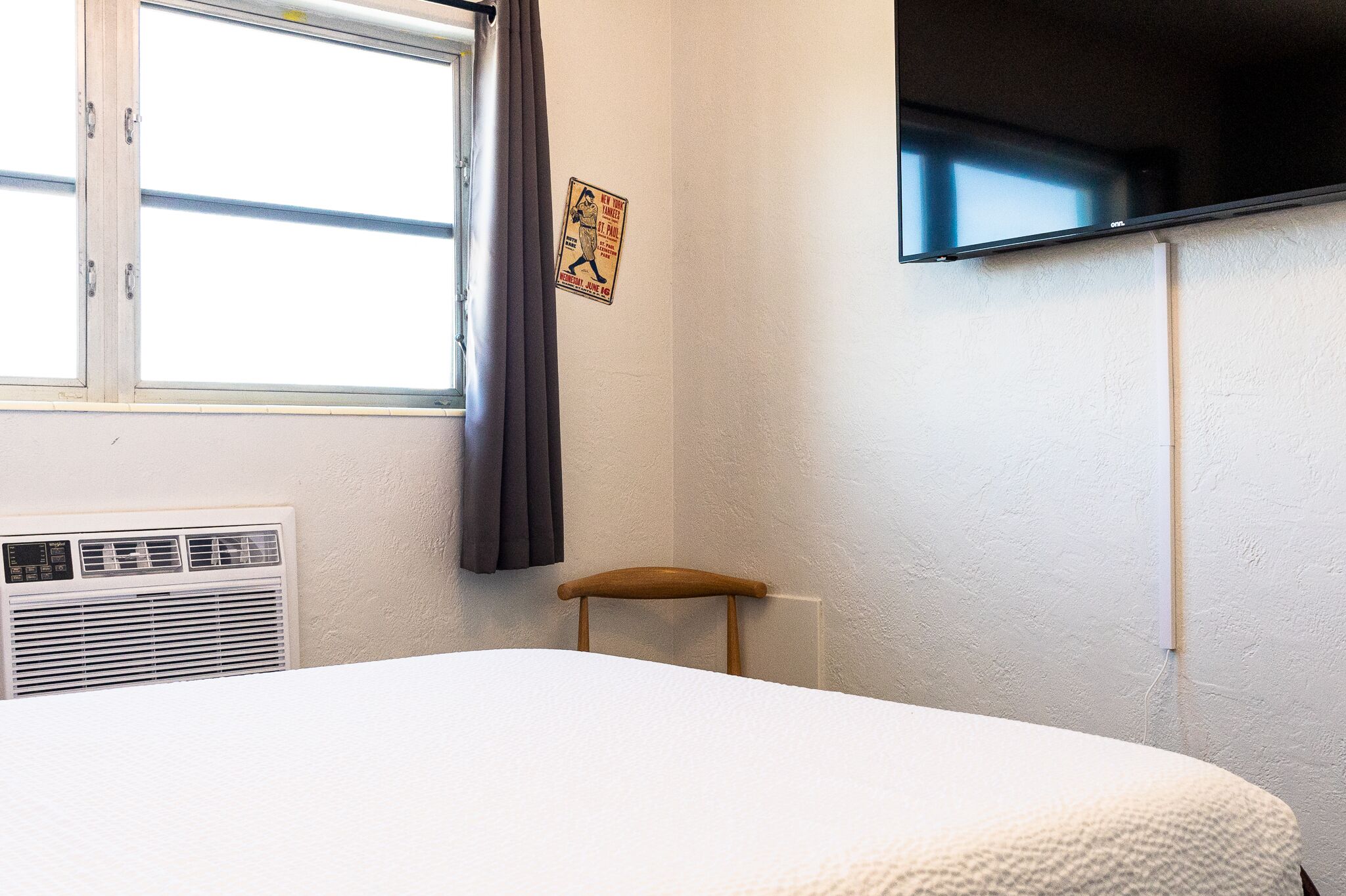 Un dormitorio con cama, ventana con cortinas, televisor montado en la pared y radiador.