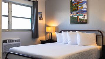 A hotel room with a bed, a window with curtains, a wall-mounted sign, and a lamp.