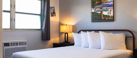 Een hotelkamer met een bed, een raam met gordijnen, een bord aan de muur en een lamp.