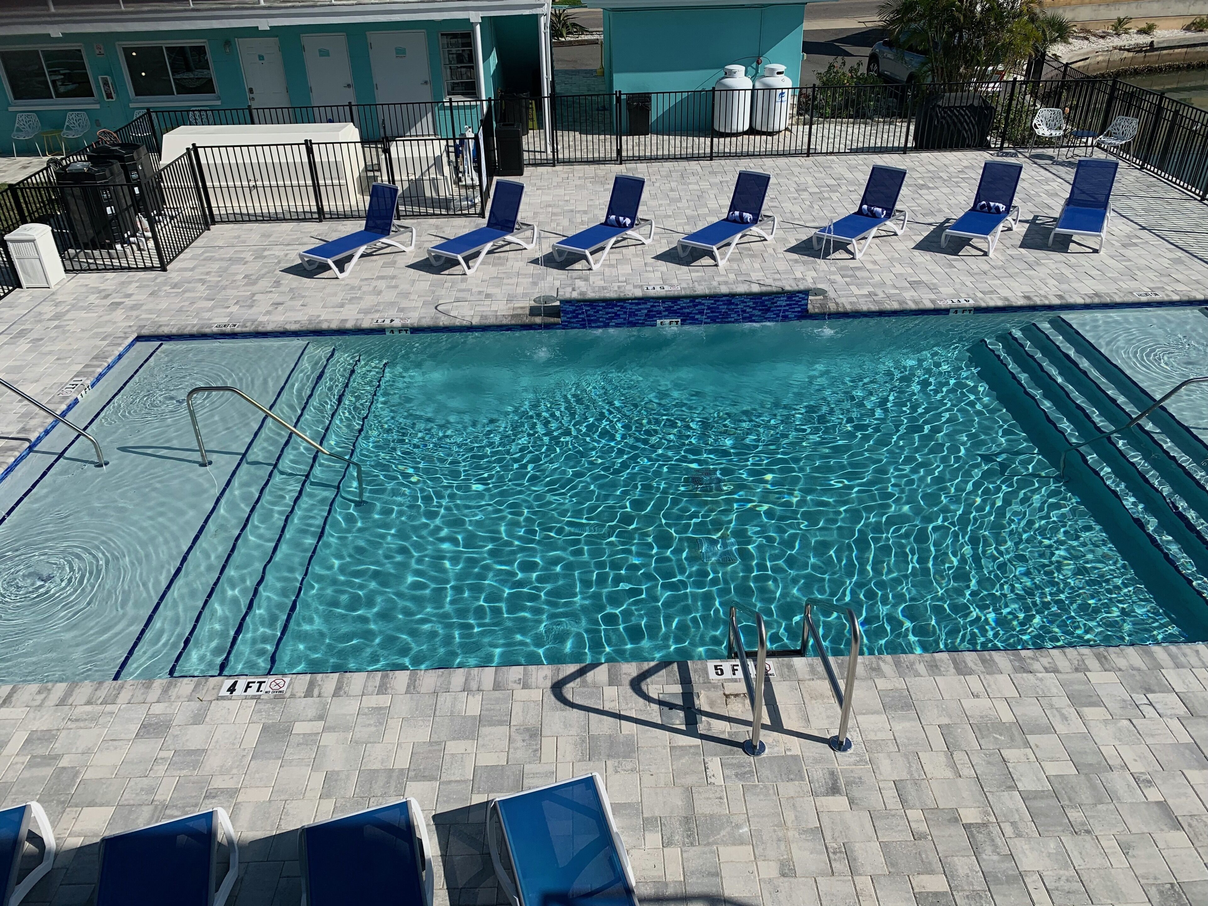 A swimming pool with clear water, surrounded by lounge chairs and a tiled deck.