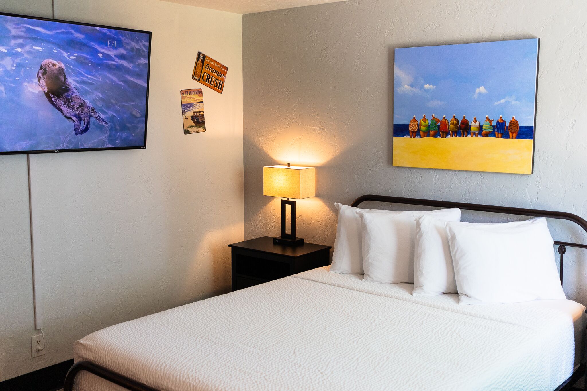 A hotel room with a bed, a TV, a painting, and a lamp.