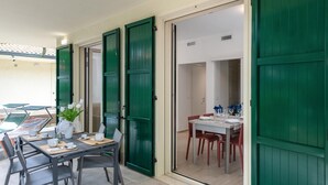 Un coin repas avec une table dressée pour deux personnes, une plante en pot et une vue sur une pièce où se trouvent une table à manger et des chaises.