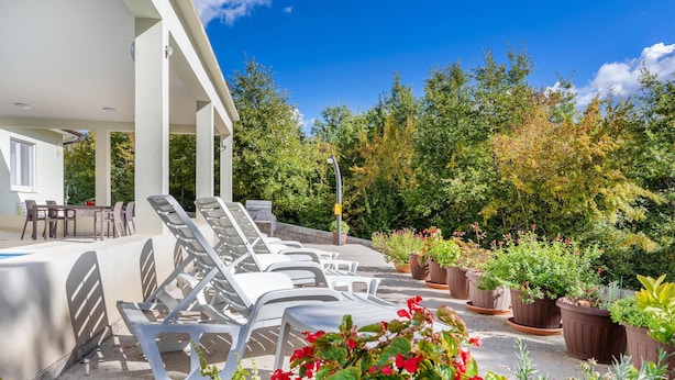 A covered outdoor seating area with lounge chairs and a table, surrounded by potted plants and trees. - Stunning home in Zminj (Zminj)
