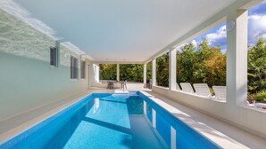A covered swimming pool with a view of trees and a patio area with chairs and a table. - Stunning home in Zminj (Zminj)