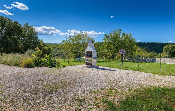 A stone outdoor grill in a grassy area with a clear sky and trees in the background. - Stunning home in Zminj (Zminj)