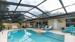 A covered outdoor swimming pool with lounge chairs and a barbecue area. - Coastal Luxury - Walk to Beach - Heated Pool (Tarpon Springs)