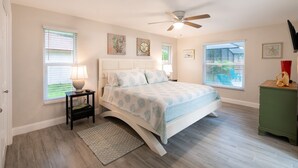 A bedroom with a bed, a nightstand, a floor lamp, a ceiling fan, and artwork on the walls. - Coastal Luxury - Walk to Beach - Heated Pool (Tarpon Springs)
