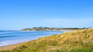 Een kustlandschap met een zandstrand, zandduinen begroeid met gras en een in de verte gelegen stadje met huizen en een heuvel.