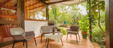 A covered patio with four chairs, a small table, and a bottle of wine.