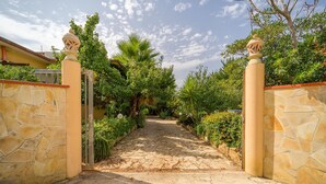 A stone pathway leading to a gated entrance surrounded by lush greenery and a clear sky. - Lovely home in Menfi with WiFi (Menfi)