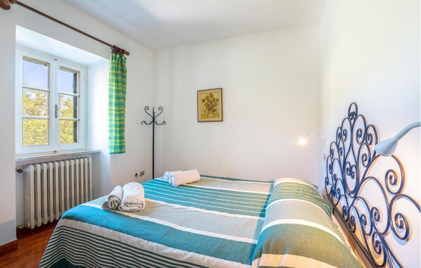 A room with two beds, a radiator, a window with curtains, a coat rack, a painting, and a decorative metal headboard. - 3 bedroom stunning home in Marciana (Marciana)