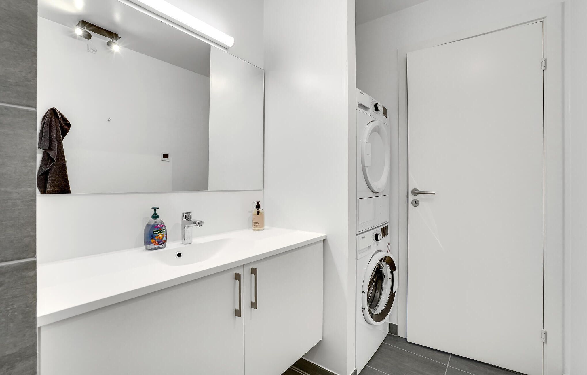 A modern bathroom with a white sink, mirror, and two washing machines.