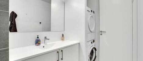 A modern bathroom with a white sink, mirror, and two washing machines.