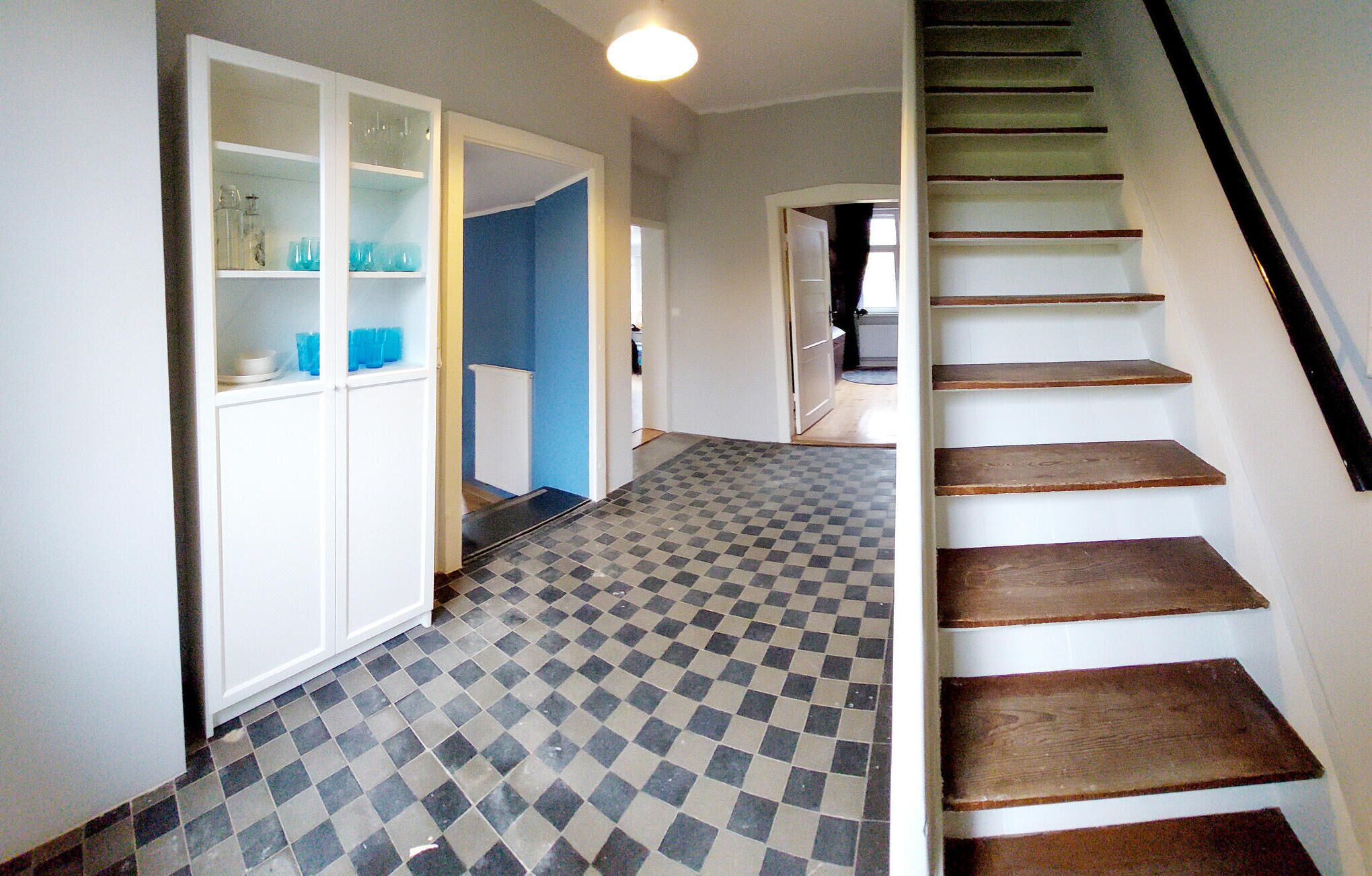 A hallway with a checkered floor, a white cabinet with glass doors, and a wooden staircase.