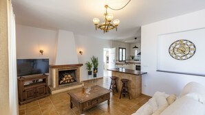 A living room with a fireplace, a TV, and a kitchen area with a bar.