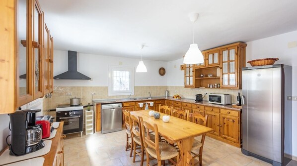 Una cucina moderna con mobili in legno, un frigorifero in acciaio inox, un tavolo da pranzo con sedie e lampade a sospensione.