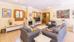 Een woonkamer met grijze banken, een witte salontafel, een open haard en houten kasten.