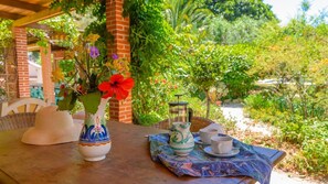 Una mesa con cafetera, tazas y un florero con flores.