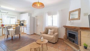 Un salon avec un canapé, une table à manger entourée de chaises, une cheminée et, au fond, un coin cuisine.