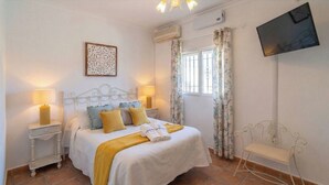 Une chambre à coucher avec un lit, des tables de chevet, une télévision et une fenêtre avec des rideaux.