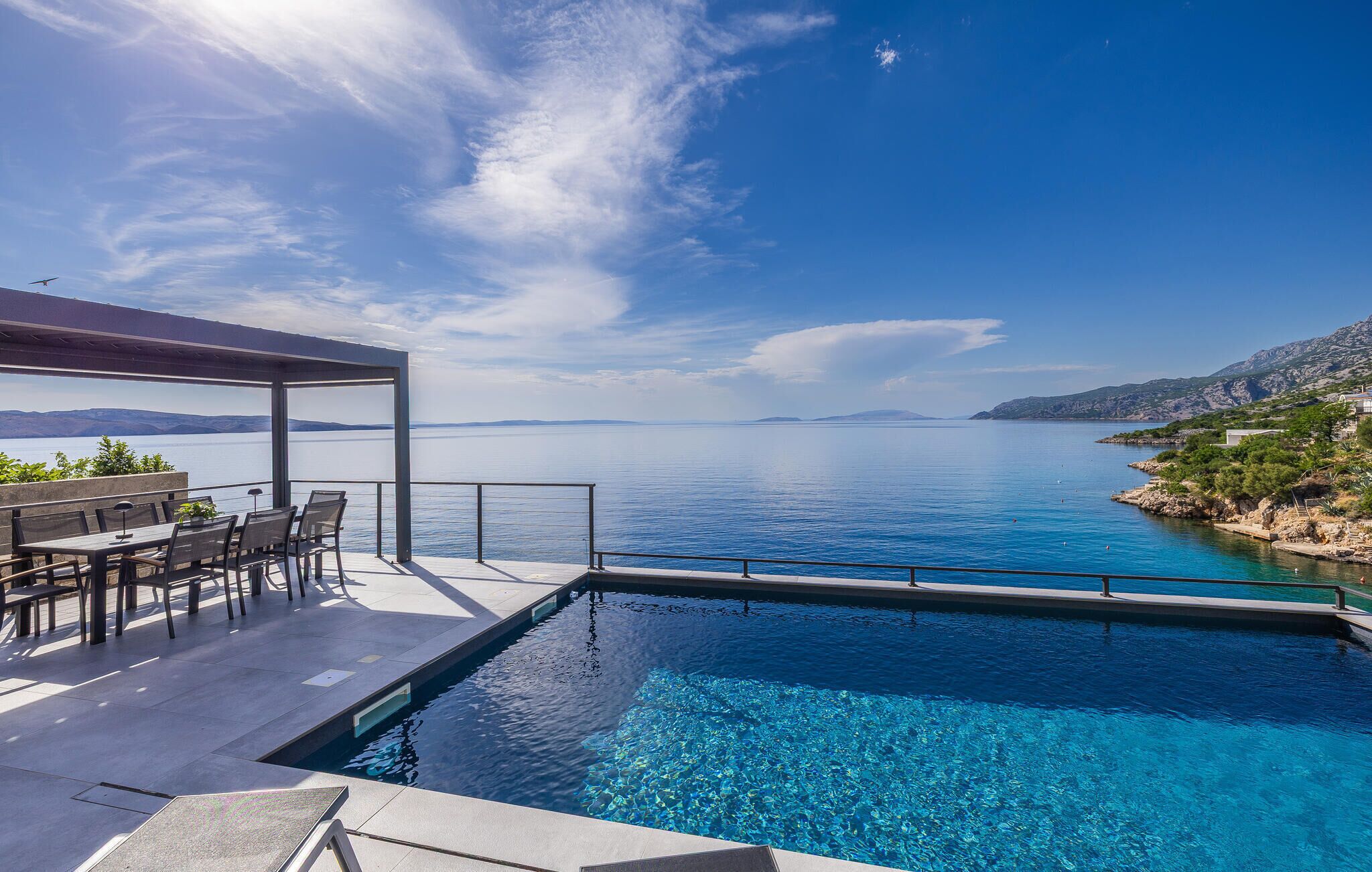 A pool with a view of a calm sea and distant mountains.