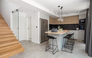 A modern kitchen with a central island, bar stools, a refrigerator, and a microwave.