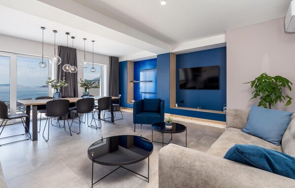 A modern living room with a dining area, a large TV, and a view of the sea.