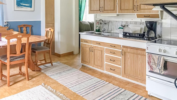A compact kitchen with wooden cabinets, a dining table with chairs, and a striped rug. - 2 bedroom cozy apartment in Boliden (Boliden)