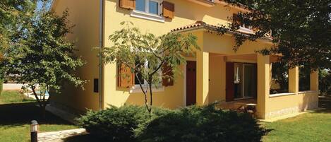 A yellow building with a tiled roof, a chimney, and a small porch with a door.