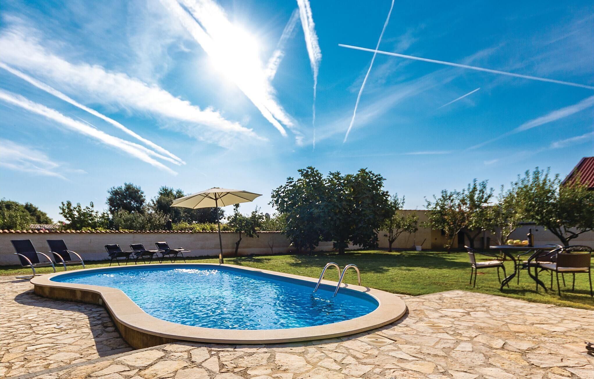 A swimming pool with a stone deck, surrounded by lounge chairs and an umbrella.
