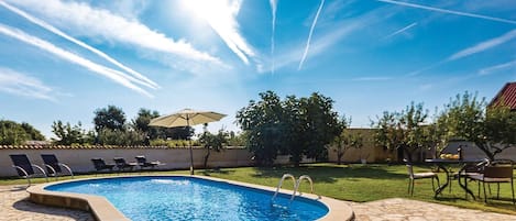 A swimming pool with a stone deck, surrounded by lounge chairs and an umbrella.