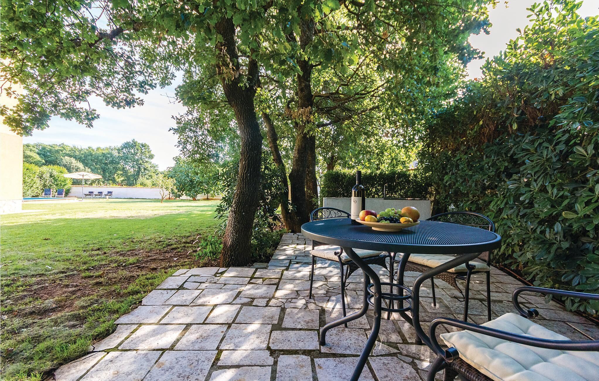 A patio with a round table and chairs, surrounded by trees and a grassy area.