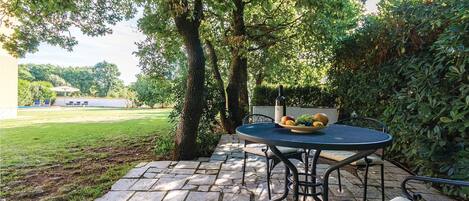 A patio with a round table and chairs, surrounded by trees and a grassy area.