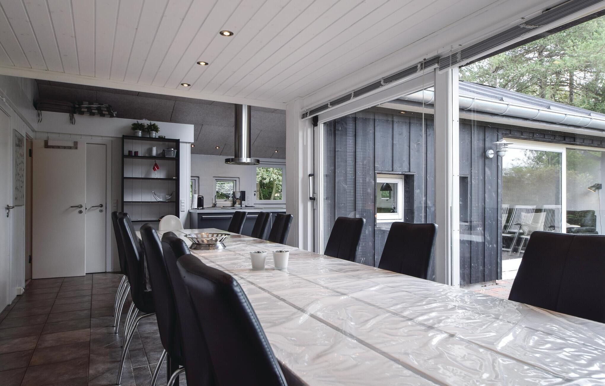 A modern dining area with a long table, black chairs, and a kitchen in the background.