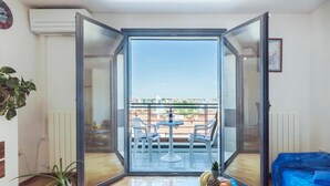 A modern apartment with a glass door leading to a balcony with a table and chairs, a potted plant, and a blue sofa. - Awesome apartment in Pula with WiFi (Pula)