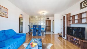 A living room with a blue sofa, a coffee table with fruit, a TV, and a dining area with chairs and a table. - Awesome apartment in Pula with WiFi (Pula)