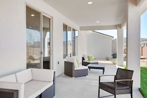Un patio coperto con mobili in vimini, ampie porte scorrevoli in vetro e vista sul paesaggio circostante.