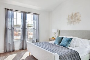 A bedroom with a bed, curtains, a nightstand, and a wall art piece.