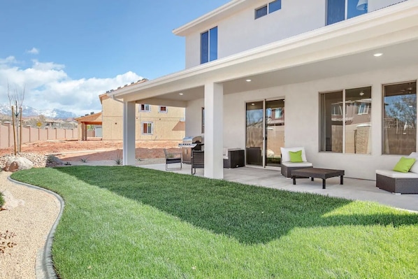 A modern house with a covered patio, outdoor seating, and a well-maintained lawn.