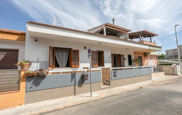 Ein modernes, zweistöckiges Haus mit flachem Dach, großen Fenstern mit Holzläden und einer überdachten Veranda.