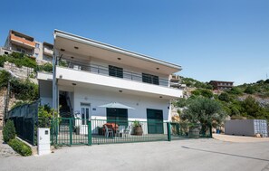 Un bâtiment à deux étages, doté d’un toit plat, d’un balcon à l’étage supérieur et d’une entrée fermée par un portail.