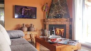 A living room with a stone fireplace, a television mounted on the wall, and a coffee table with a bottle of wine, glasses, and a bowl of strawberries. - Nice home in Algatocin (Algatocin)