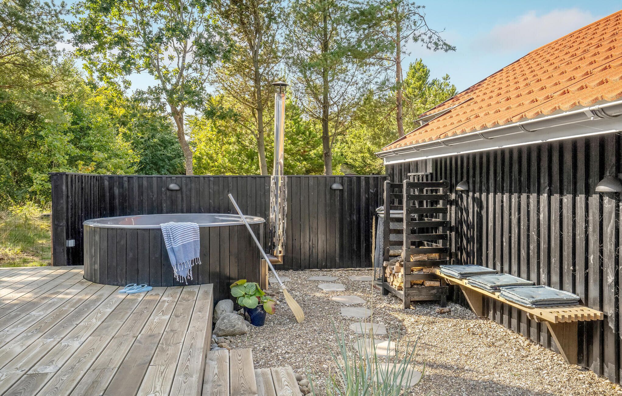 Een houten terras met een jacuzzi, een houten bank en een pergola met dak.