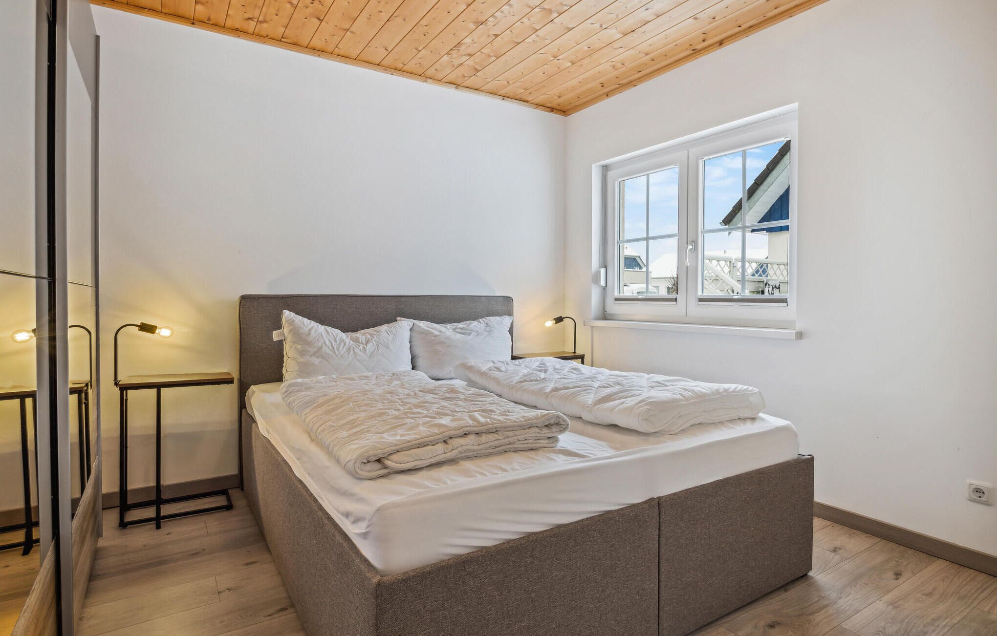A bedroom with a bed, bedside lamps, a window, and a view of the outside.