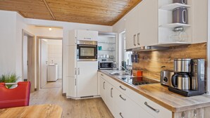 A modern kitchen with white cabinets, stainless steel appliances, and a wooden ceiling. - Ferienwohnung Altefähr (Altefähr/Rügen)