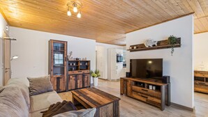 A modern living room with a wooden ceiling, a large TV, and a built-in wooden cabinet. - Ferienwohnung Altefähr (Altefähr/Rügen)