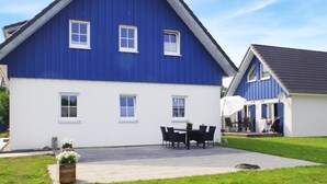 A two-story house with a blue exterior and white trim, a patio with a table and chairs, and a small garden area. - Ferienwohnung Altefähr (Altefähr/Rügen)